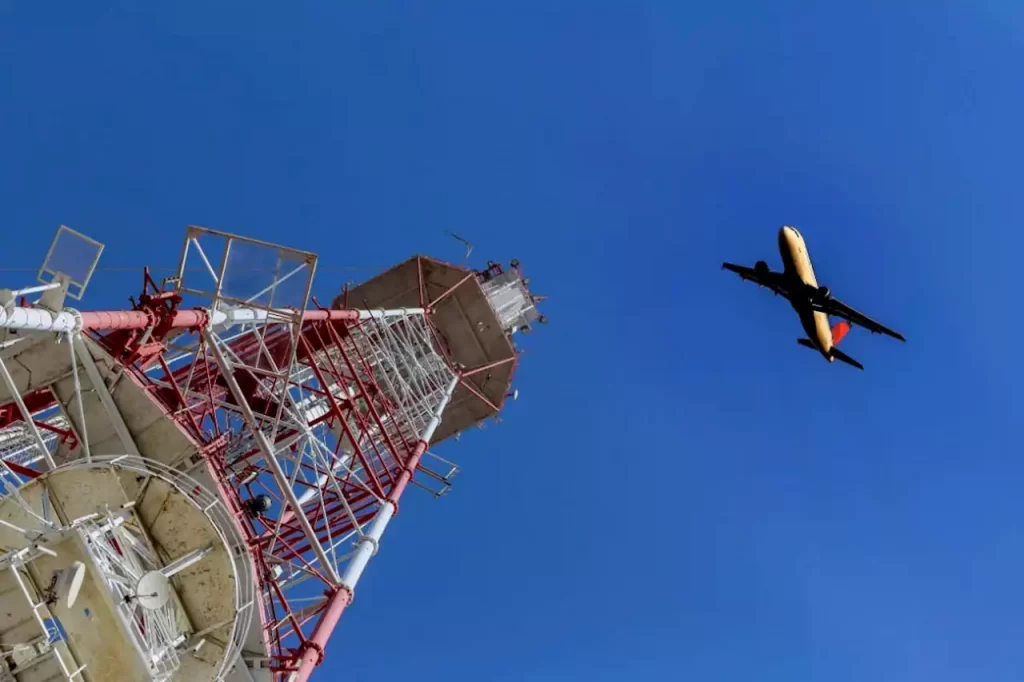 Башня аэропорта и летящий по диагонали самолёт на фоне синего неба